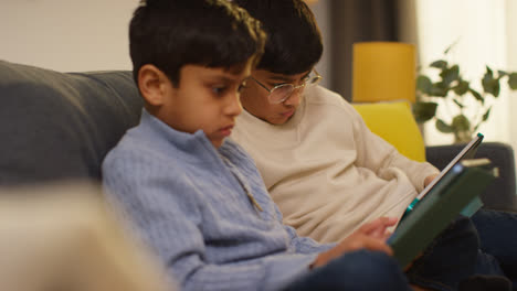 Two-Young-Boys-Sitting-On-Sofa-At-Home-Playing-Games-Or-Streaming-Onto-Digital-Tablets-21